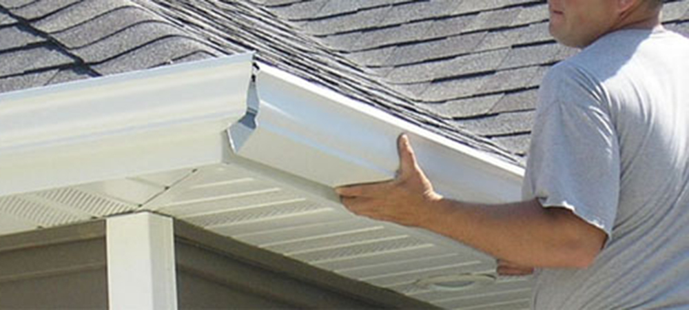 This image shows a person in a white shirt installing or positioning white gutters on a house with asphalt shingle roofing.RetryClaude can make mistakes. Please double-check responses.